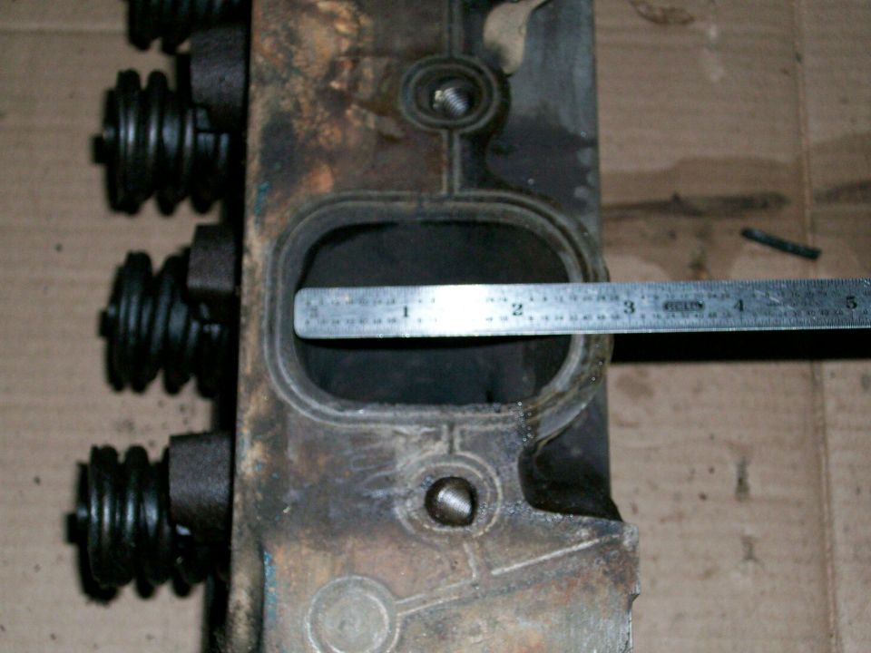Close-up of an engine cylinder head with valve springs and a ruler measuring an intake port