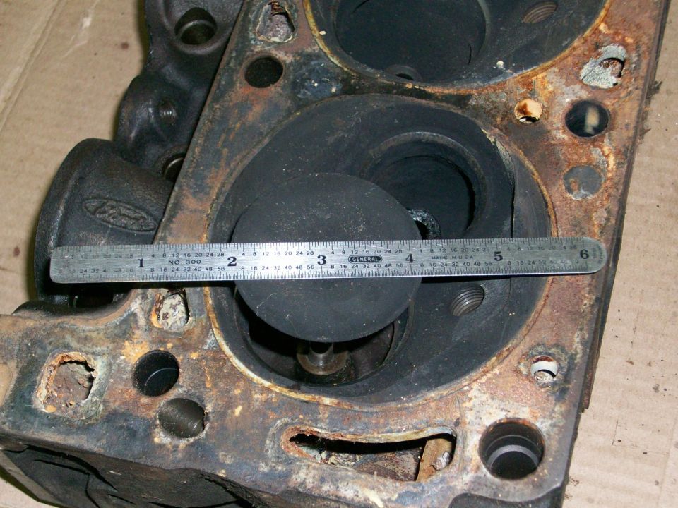 Close-up of a rusty engine cylinder head with a ruler measuring the valve opening