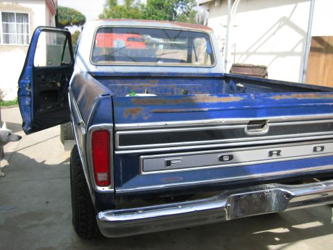1979 Ford F-150 - Blue Ford F-150 pickup truck, driver's door open, showing rear tailgate and bed. Rust is present.