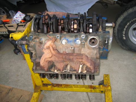 1979 Ford F-150 - Engine block on a yellow stand with visible internal components and a rusty exhaust manifold.