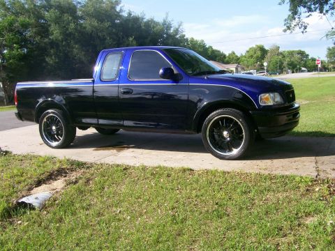 1997 Ford F-150 - This two-tone pickup truck is viewed from its right side, showing its custom wheels and body style.
