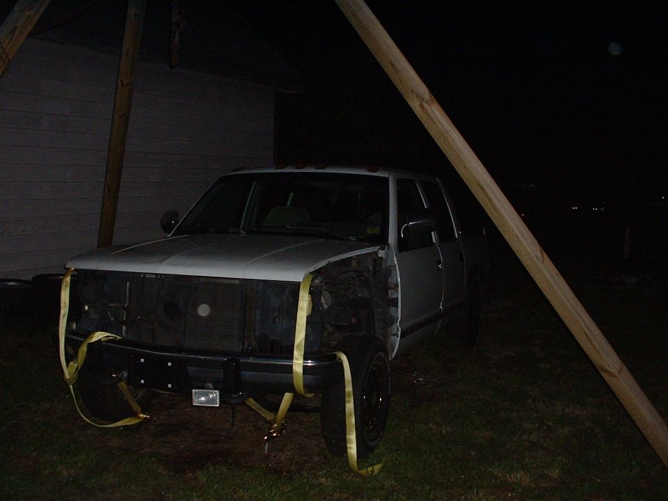 Silver crew-cab pickup truck at night with front bumper removed