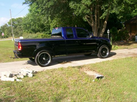 1997 Ford F-150 - This 1997 Ford F-150 pickup truck is shown from the side, a two-tone black and blue paint scheme and aftermarket wheels.