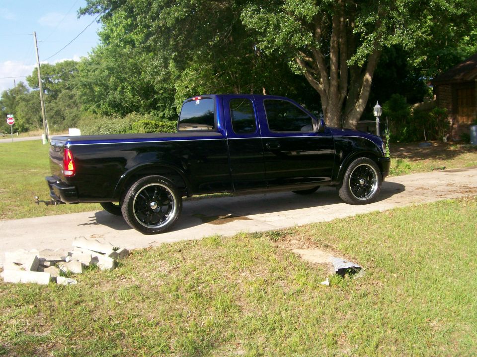 Side view of black and blue 1997 Ford F-150 pickup truck with custom wheels