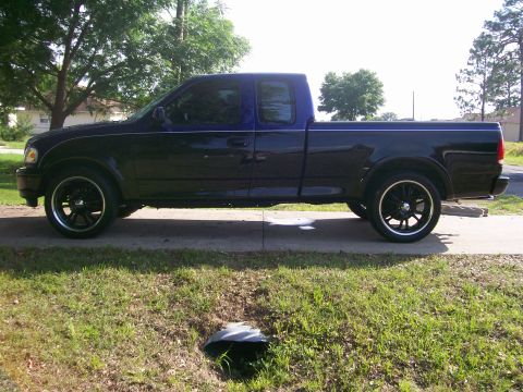 1997 Ford F-150 - This truck has a dark body with a contrasting blue top section and aftermarket wheels.
