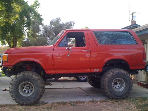 1969 Ford F-250 - This lifted red Ford Bronco has 4x4 badging on the side. A second vehicle is visible behind it.
