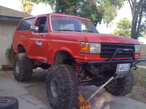 1969 Ford F-250 - This heavily modified red Ford Bronco sits on a jack, its lifted suspension and massive off-road tires.