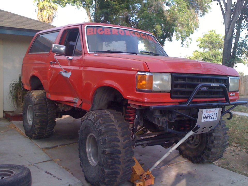 Red Ford Bronco lifted with large tires, front bumper, and "BIG BRONCO GIRL" sticker on windshield