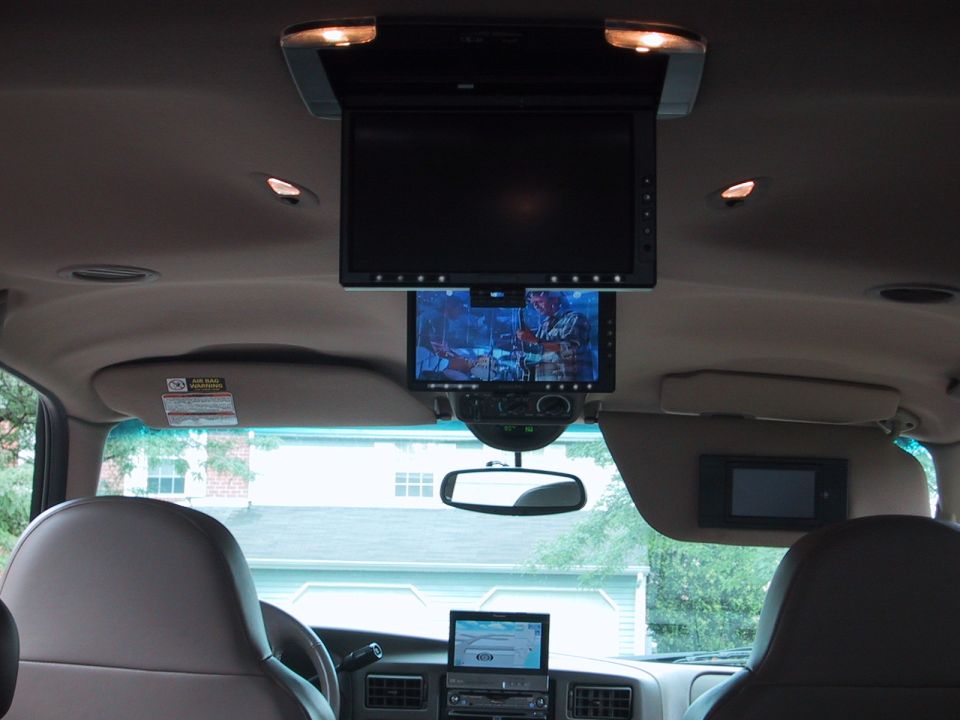Tan SUV interior with multiple overhead flip-down video screens and an in-dash display
