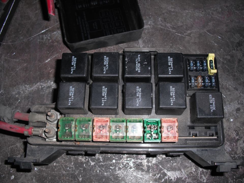 Automotive fuse box with multiple relays and fuses. Some fuses are green, orange, and clear