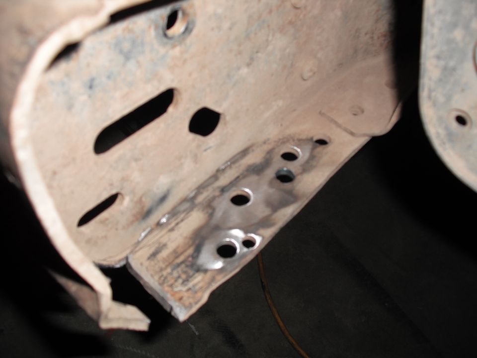 Rusted metal frame section with multiple drilled holes and signs of welding