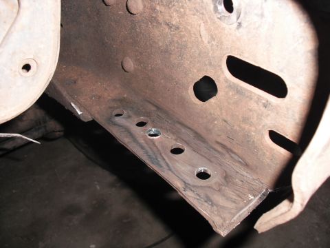 1991 Ford Bronco - Close-up view of a rusted metal frame section showing several drilled holes.