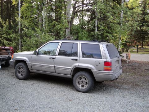1990 Chevrolet Suburban - A silver SUV is parked on a gravel lot with trees in the background.