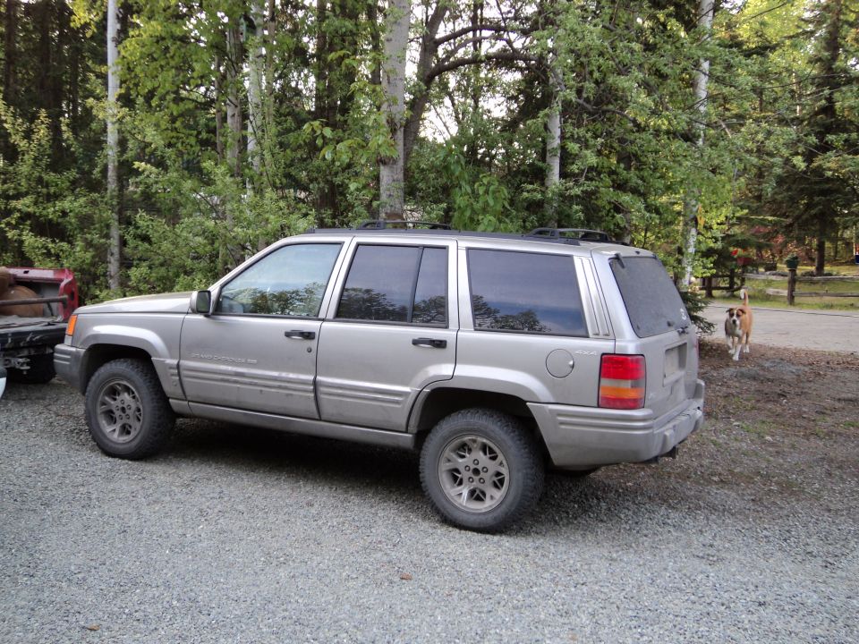 Silver SUV parked on gravel, side view. Appears to be a Jeep Grand Cherokee from the 1990s