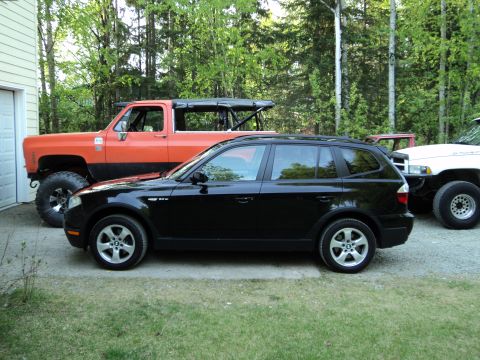 1990 Chevrolet Suburban - A black BMW X3 is parked in front of an orange lifted Chevrolet pickup truck.