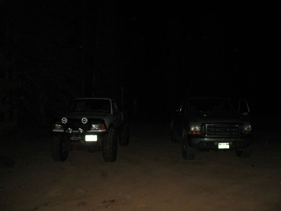 two trucks parked outside at night, one on the left has extra lights on the front bumper