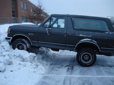 1988 Ford Bronco - A 1988 Ford Bronco navigates a snowy parking lot near a brick building.