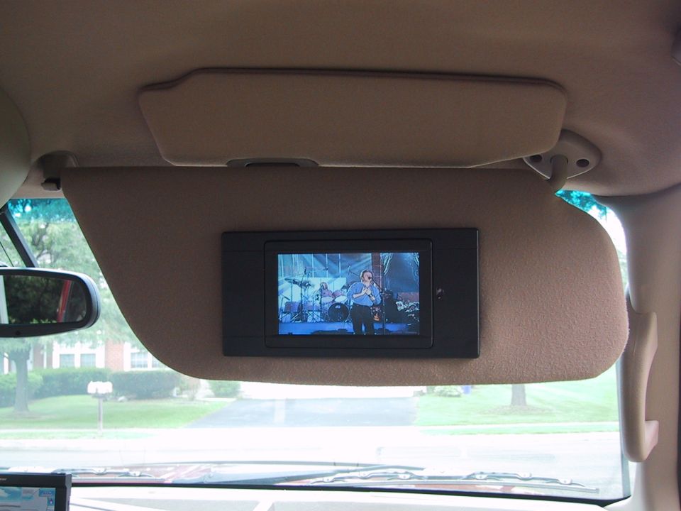 Tan sun visor with built-in black LCD screen playing video inside a vehicle