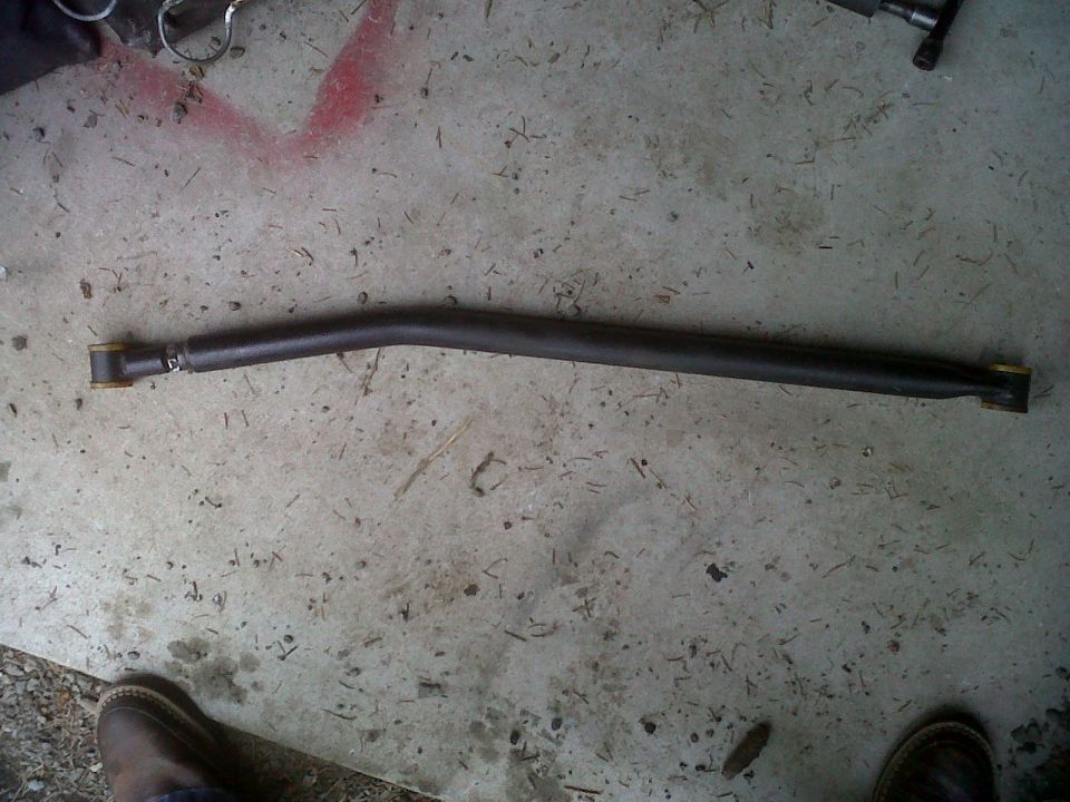 Curved metal bar with yellow bushings on ends, lying on concrete