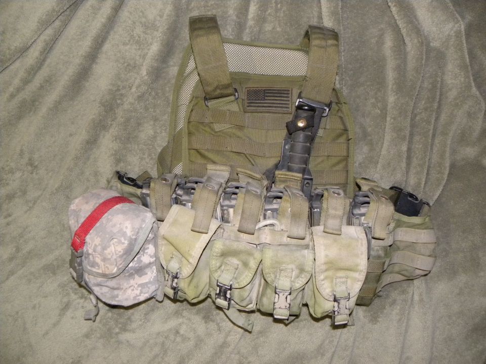 Olive drab tactical vest with multiple pouches, an American flag patch, and a red-strapped pouch