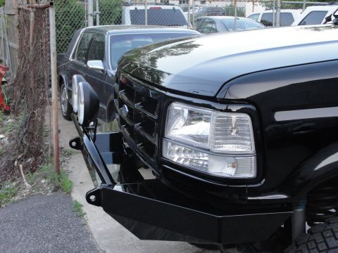 1995 Ford Bronco - Close-up of a black truck's front end, a custom bumper and grille, with another vehicle visible in the background.
