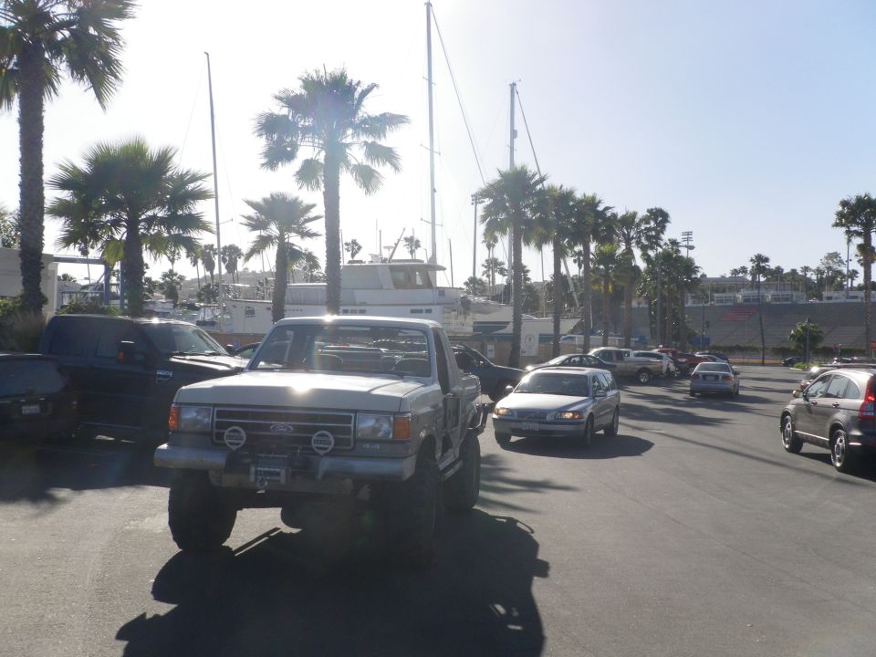 Lifted Ford F-Series pickup truck with aftermarket lights, parked near a marina with sailboats