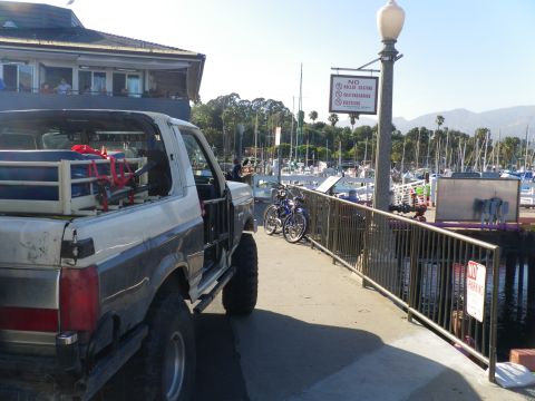 1991 Ford Bronco - A two-tone Ford Bronco is parked on a pier next to a marina with sailboats in the background.