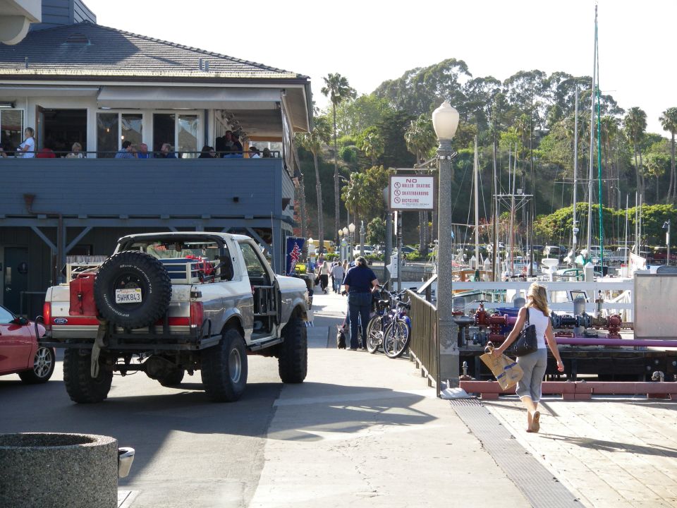 Silver Ford Bronco with spare tire on back, off-road modifications, parked near a marina