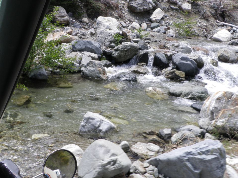 view of a rocky stream bed with water flowing over rocks, seen from inside a vehicle
