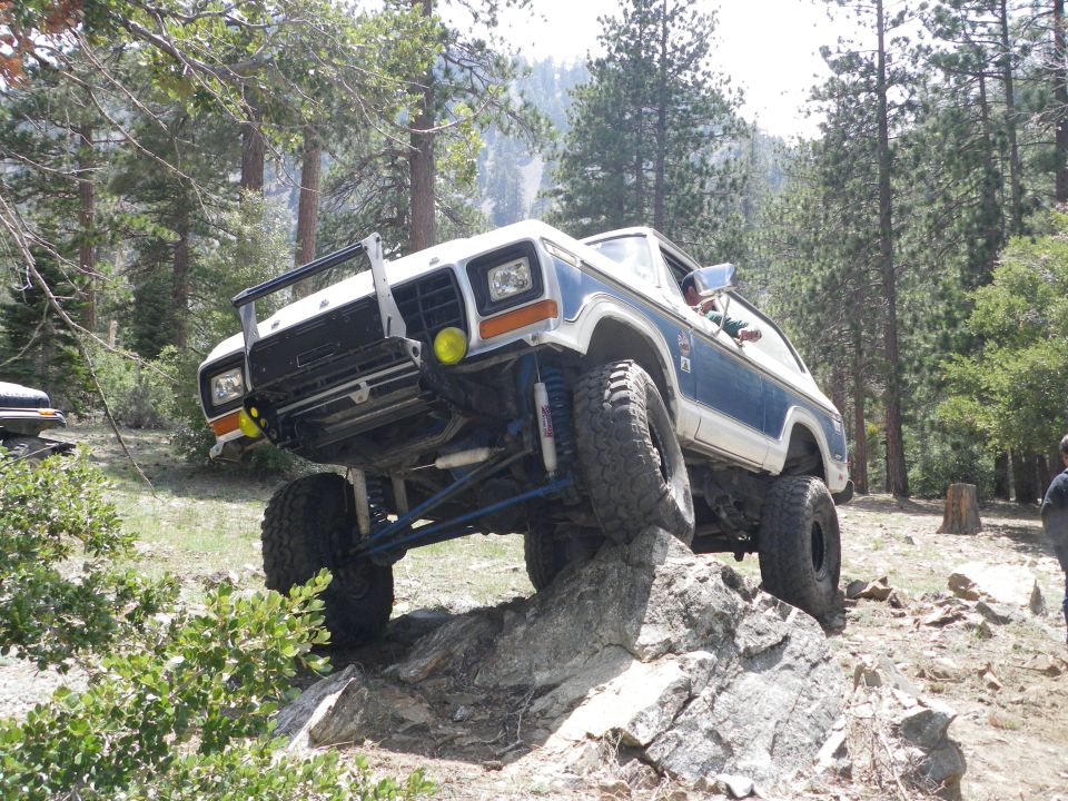 Modified Ford Bronco climbing over rocks on a trail, front end lifted high