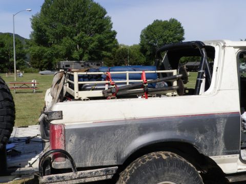 1991 Ford Bronco - A white Ford Bronco is packed with gear on a cargo rack, ready for an outdoor adventure.