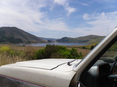 1991 Ford Bronco - View from inside a white SUV overlooks a lake surrounded by rolling hills under a cloudy sky.
