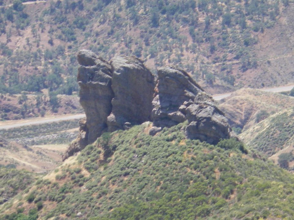 Rock formation on a green, hilly landscape with a road in the background