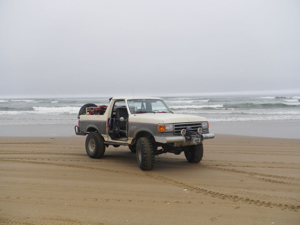 Ford Bronco parked on a sandy beach with ocean waves in the background