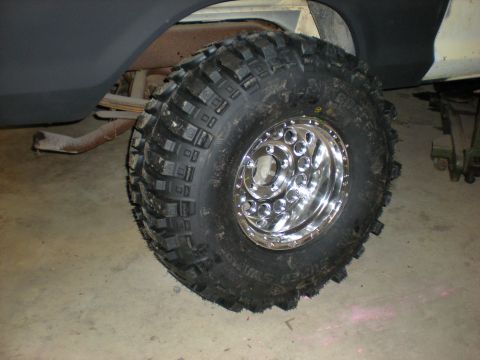 1978 Ford Bronco - A close-up view of a vehicle's rear wheel and tire assembly, showing off-road tread and a polished chrome rim.