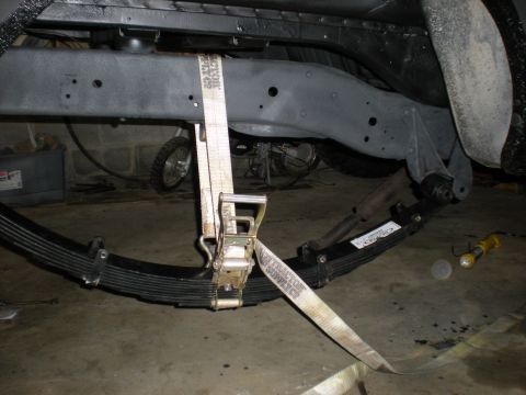 1978 Ford Bronco - Close-up of vehicle frame and suspension components with a ratchet strap attached.