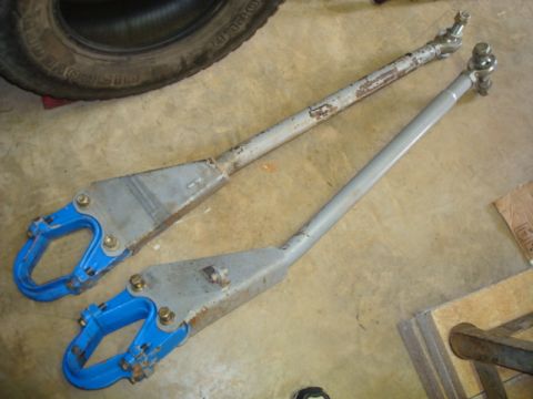1995 Ford Bronco - Two steering tie rods, one with a worn metal finish and the other painted gray, are laid out on a concrete floor.