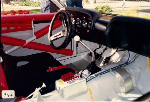 1973 Ford Mustang - The interior of a race car features a roll cage, racing seat, and a floor-mounted shifter with multiple gauges on the dashboard.