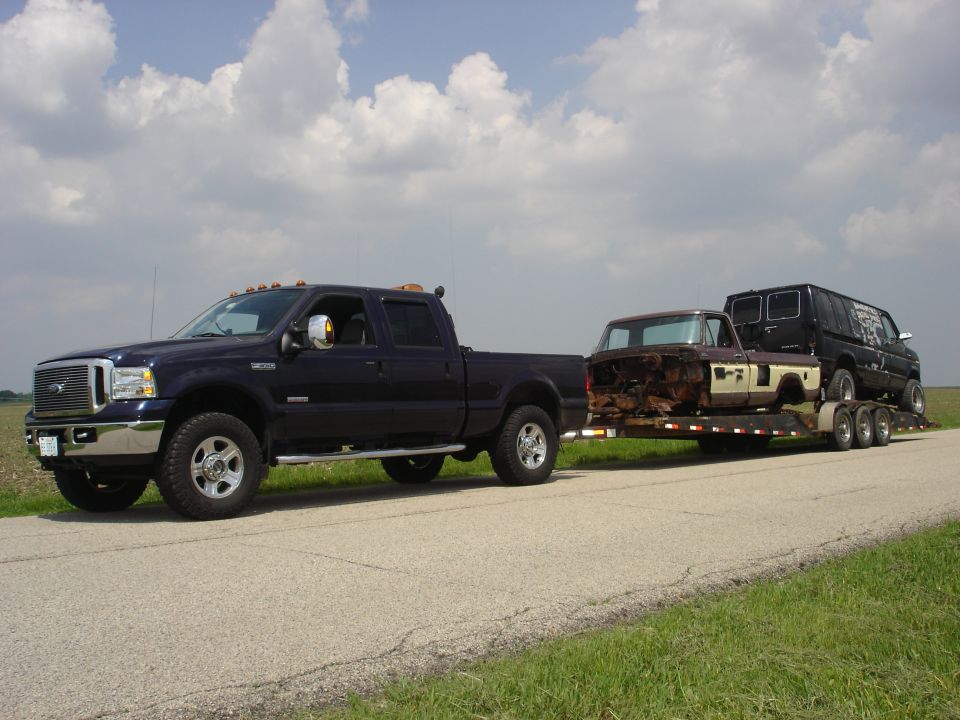 Dark blue pickup truck towing a trailer with a rusty pickup body and a black van
