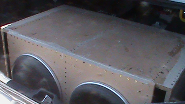 Riveted metal box with circular openings, possibly a fuel tank or storage