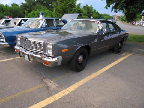 1991 Ford LTD Crown Victoria - gray vintage Dodge police sedan with chrome bumpers parked at an angle in a yellow-striped lot beside other cruisers.