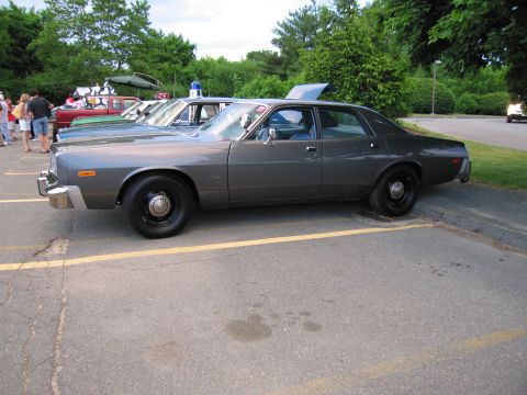 1991 Ford LTD Crown Victoria - gray vintage Dodge police sedan shown in side profile beside other cruisers with trunks open in a striped parking lot.