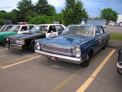 1991 Ford LTD Crown Victoria - blue Ford Galaxie 500 police sedan with trunk open parked beside a black-and-white police cruiser in a striped lot.