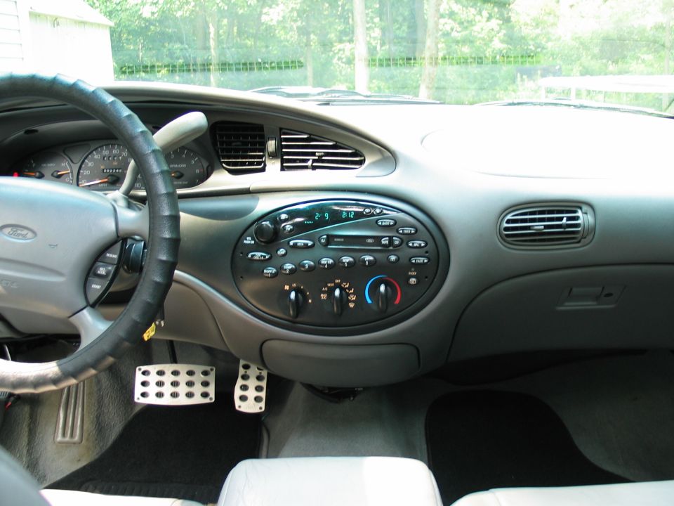 Gray dashboard and center stack of a Ford sedan with leather-wrapped wheel and drilled alloy pedals