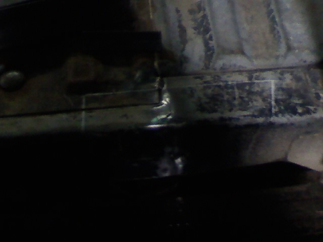 Darkened frame rail with visible welds and rectangular cutouts