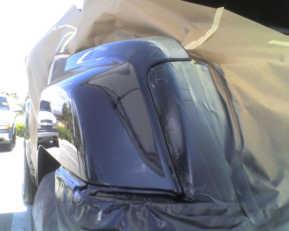 Dark rear bumper and fender covered in masking paper and tape