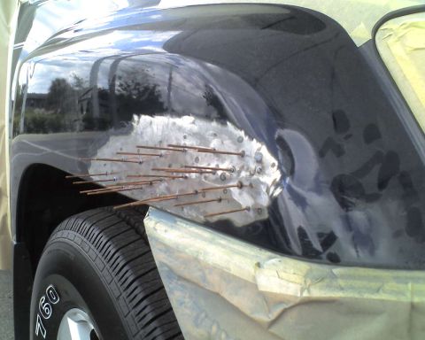 1993 Ford C-350 (Centurion Conversions) - A vehicle's fender is undergoing repair work, with numerous small metal rods attached to the damaged area.