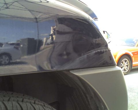 1993 Ford C-350 (Centurion Conversions) - Close-up of a damaged dark blue vehicle fender with an orange car visible in the background.