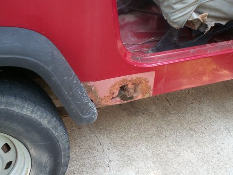1988 Jeep YJ - This red Jeep YJ shows extensive rust damage on its lower body panel, indicating a need for repair.