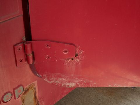 1988 Jeep YJ - Close-up of a red Jeep YJ door hinge showing signs of rust and partial lettering on the body panel.